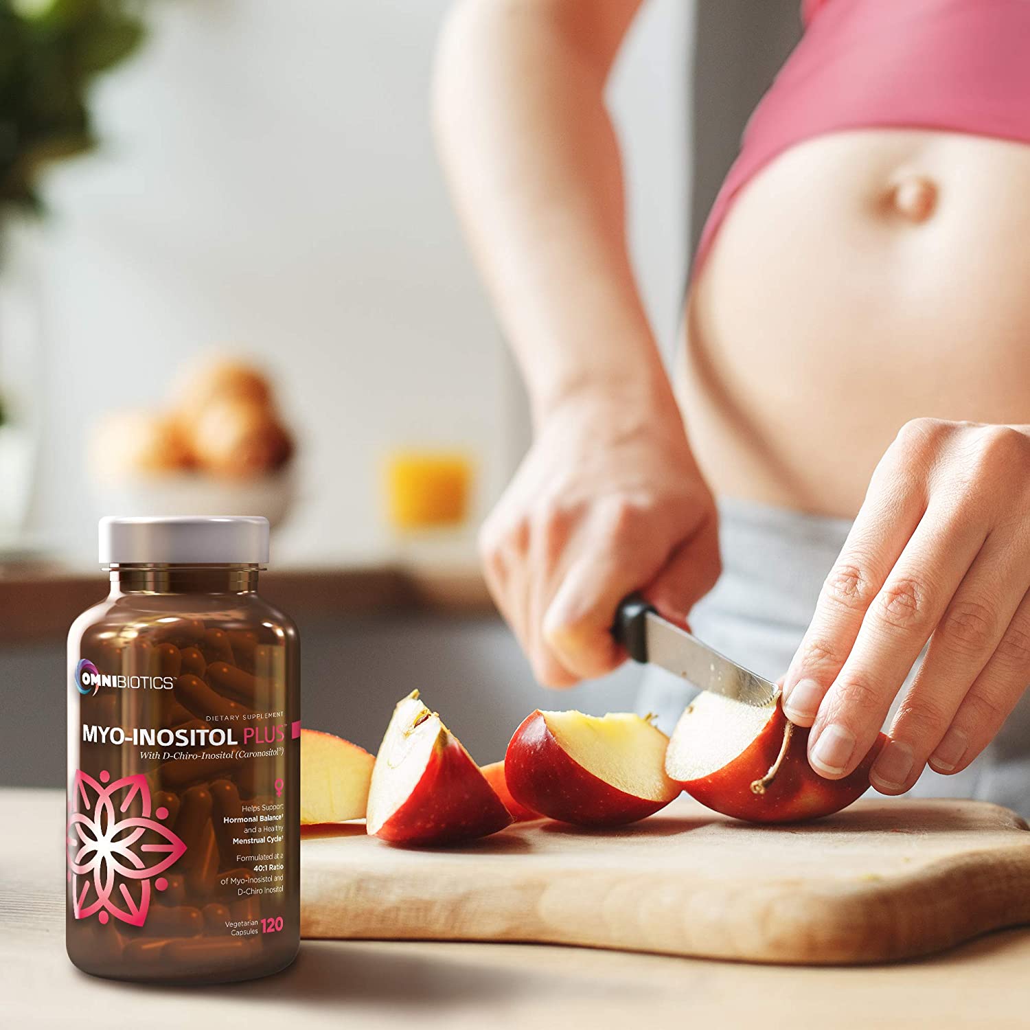 A woman is cutting apples while a bottle of Omnibiotics Myo-Inositol Plus sits on the counter beside her.
