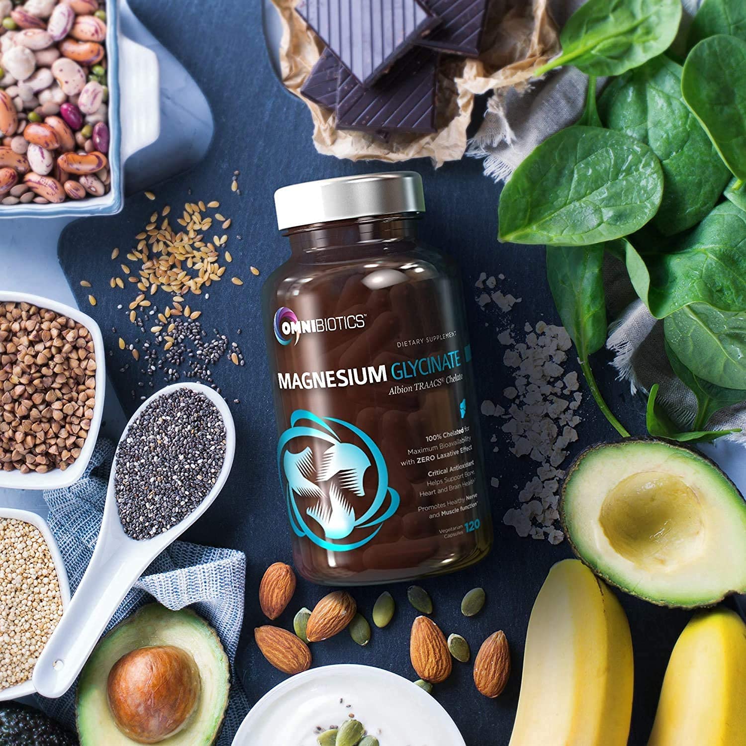 Omnibiotics Magnesium Glycinate Supplement surrounded by a colorful assortment of healthy foods featuring nuts, seeds, and dark chocolate arranged on a wooden surface.