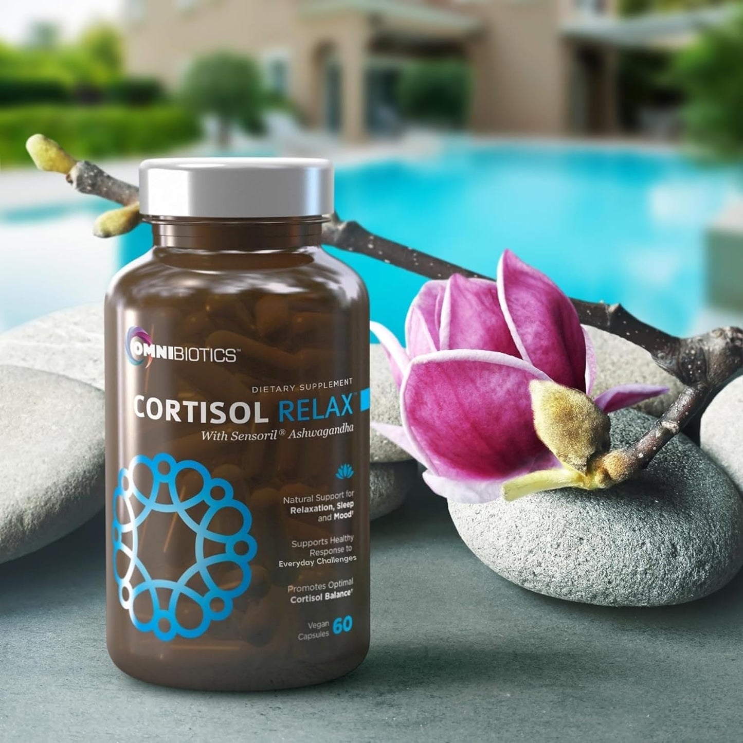 OmniBiotics Cortisol Relax with Sensoril Ashwagandha bottle beside spa stones and pink magnolia near a pool.